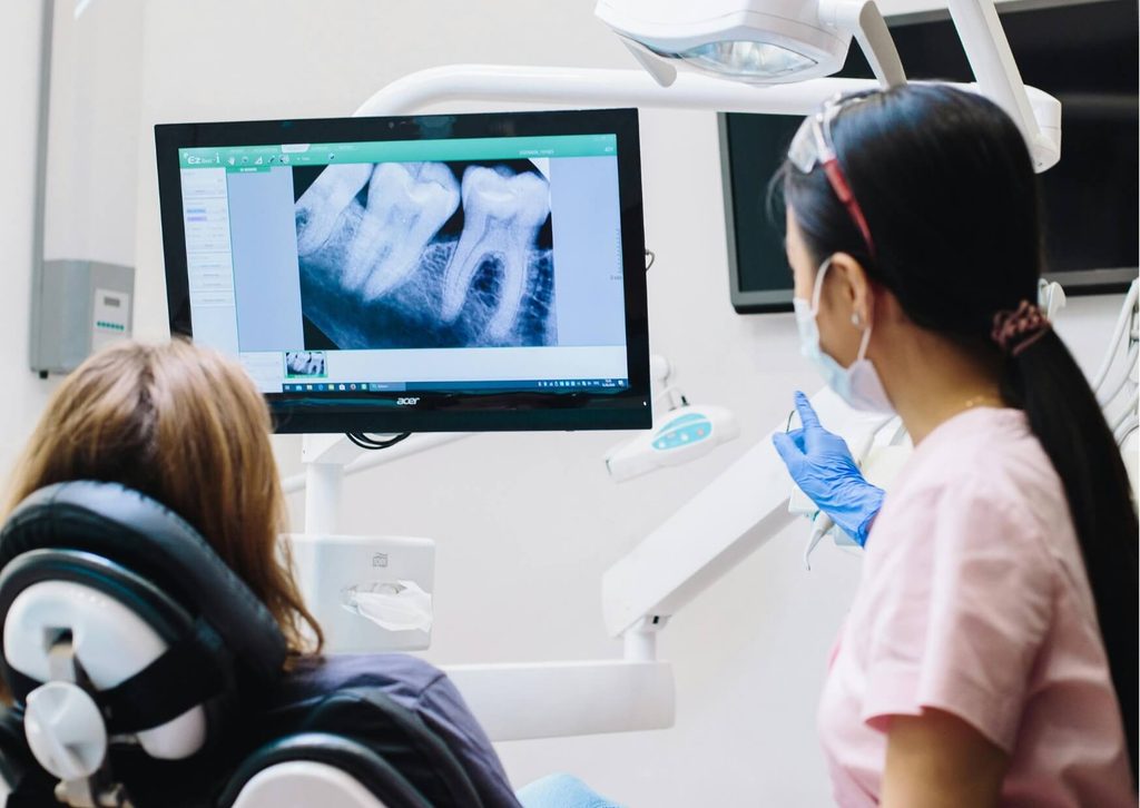 Dentist reviewing a dental X-ray with a patient before wisdom teeth extraction.
