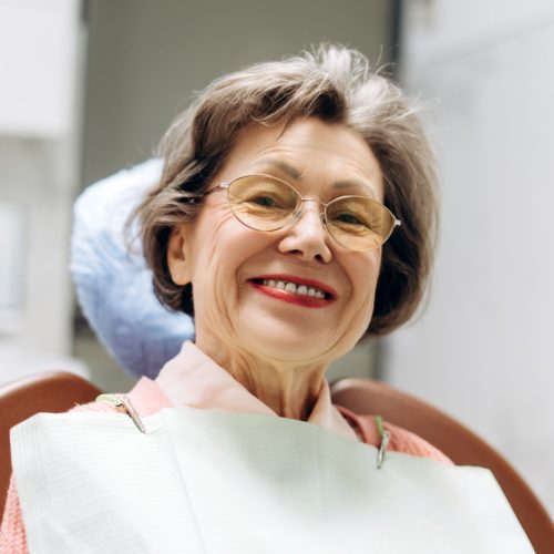 A senior woman smiles at the camera in her dentist's office- naccid, buford dentist, ga