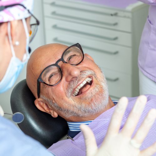 A senior man reclined in a dental chair smiles at his dentist - naccid, buford dentist, ga